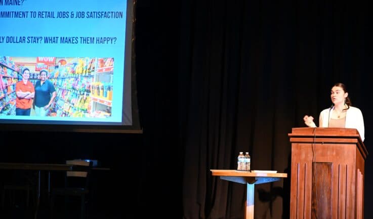 A student stands at a podium while showing a presentation in Fox Auditorium
