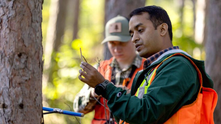 Professor Libin Louis works with a student in the forest