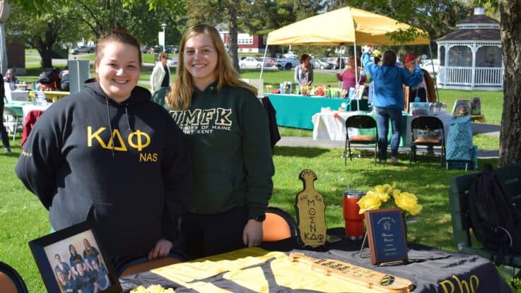 two female students from Kappa Delta Phi national affiliated sorority pose at a table during an open house event