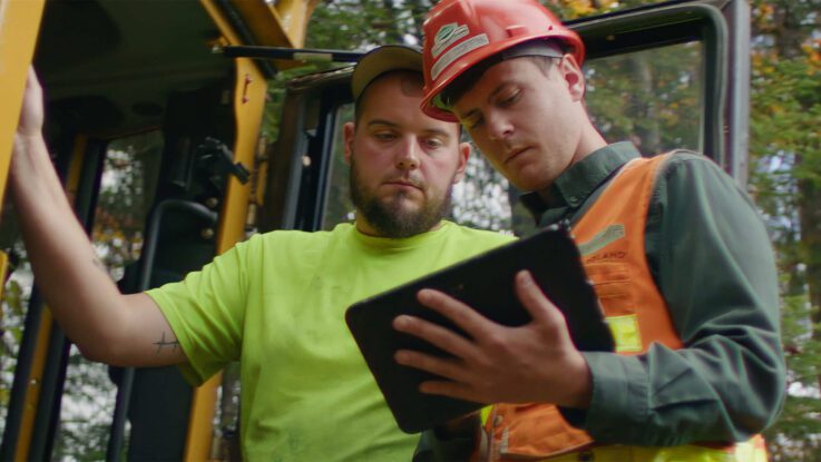 two forestry professionals on foresting equipment looking at a tablet computer