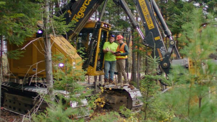 Bryce Coffin, UMFK class of 2021, talks with an employee while standing in the woods near a feller buncher