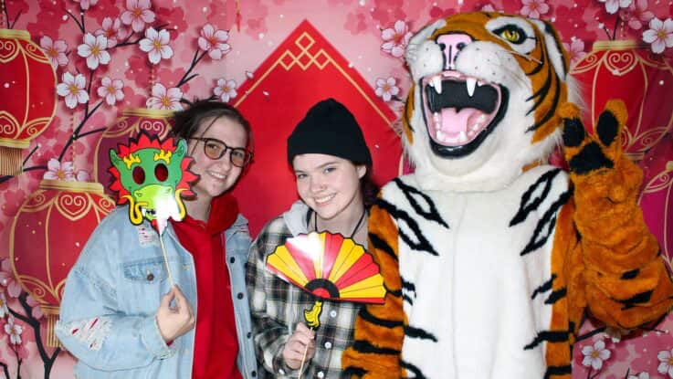 two female students, one with a mask and the other with a fan, pose with Benny the Bengal for a photo during a lunar new year event