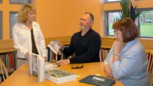 a male author and two women converse during a book signing event