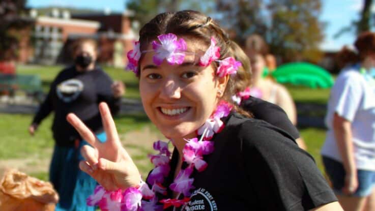 a female student wearing a lei and flower crown poses showing a peace sign during an on-campus luau