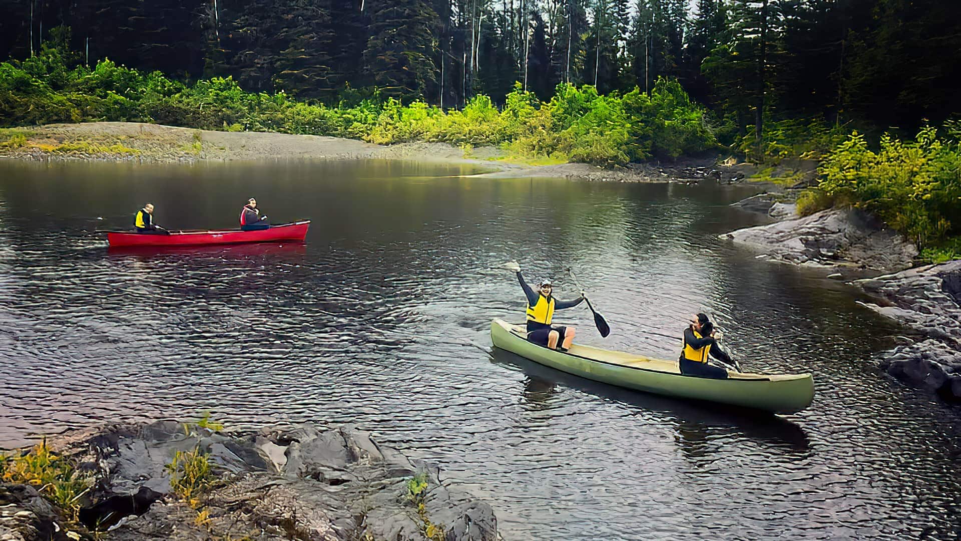 UMFK students canoeing on the river in two canoes. one student waves to the camera