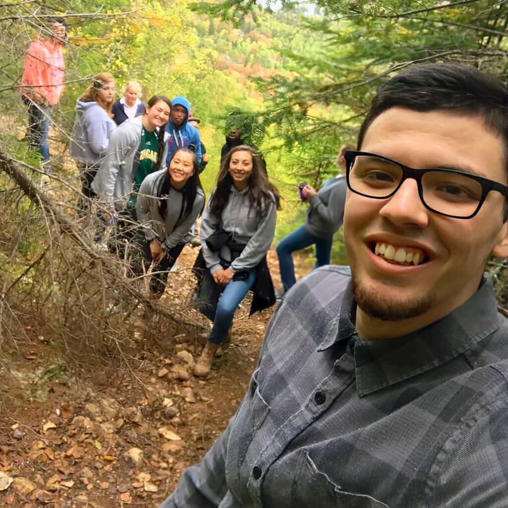 student take a group selfie on a trail overlooking a lake