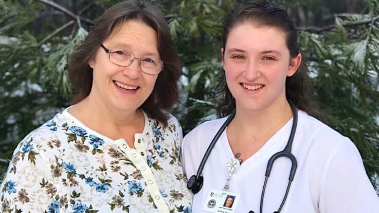 a nursing student in scrubs and stethoscope around her neck poses with a fellow nurse