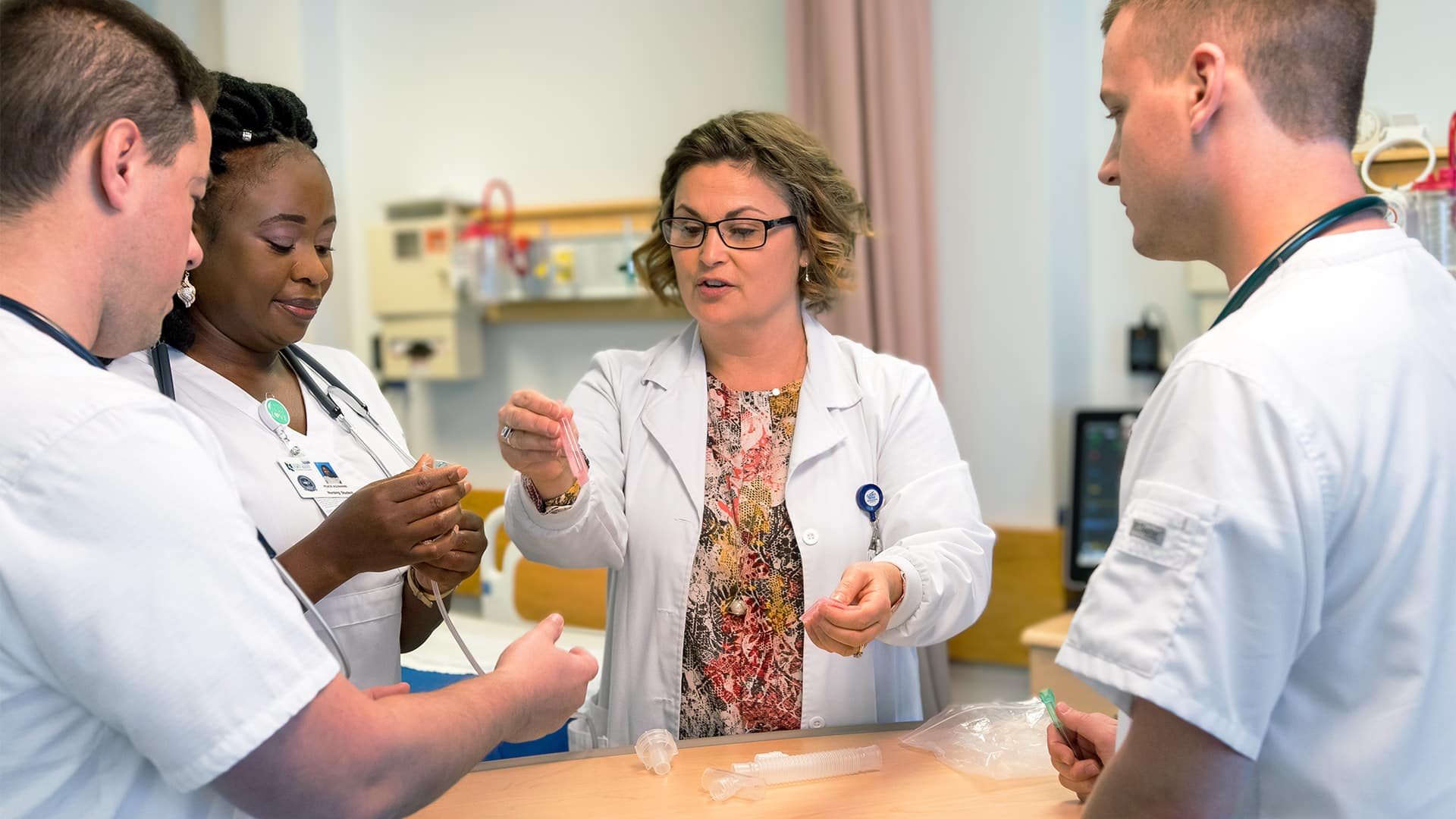 two male and one female nursing student are instructed by one of the nursing faculty