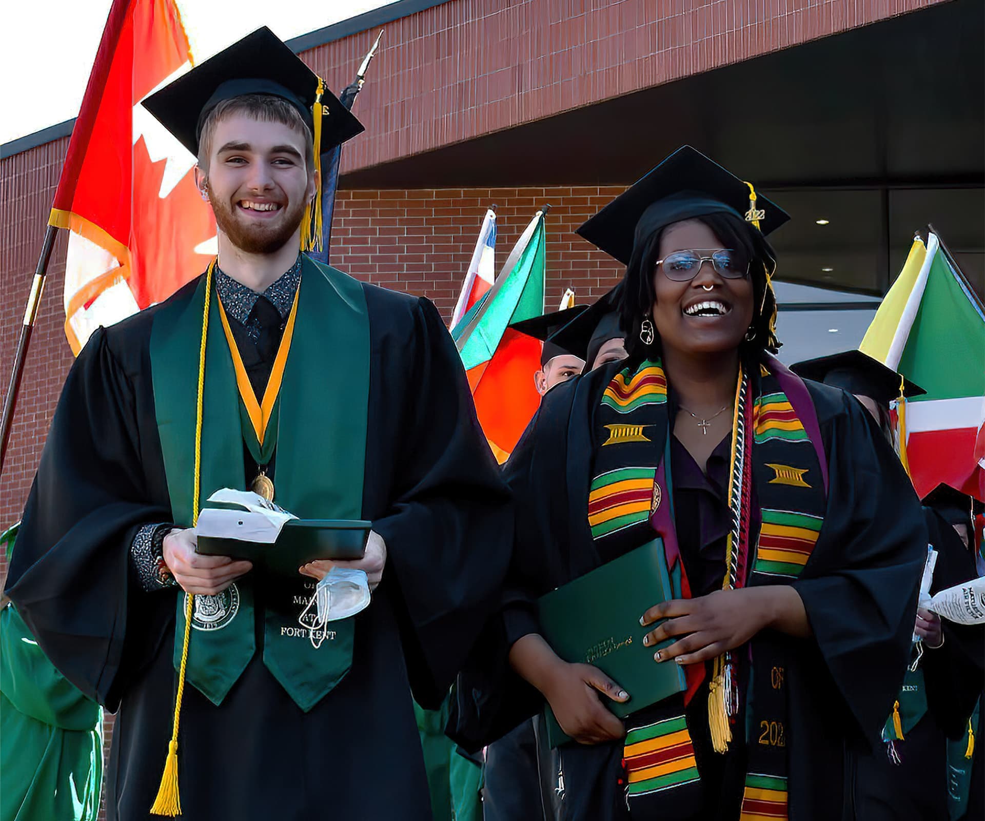 two graduates with flags behind them