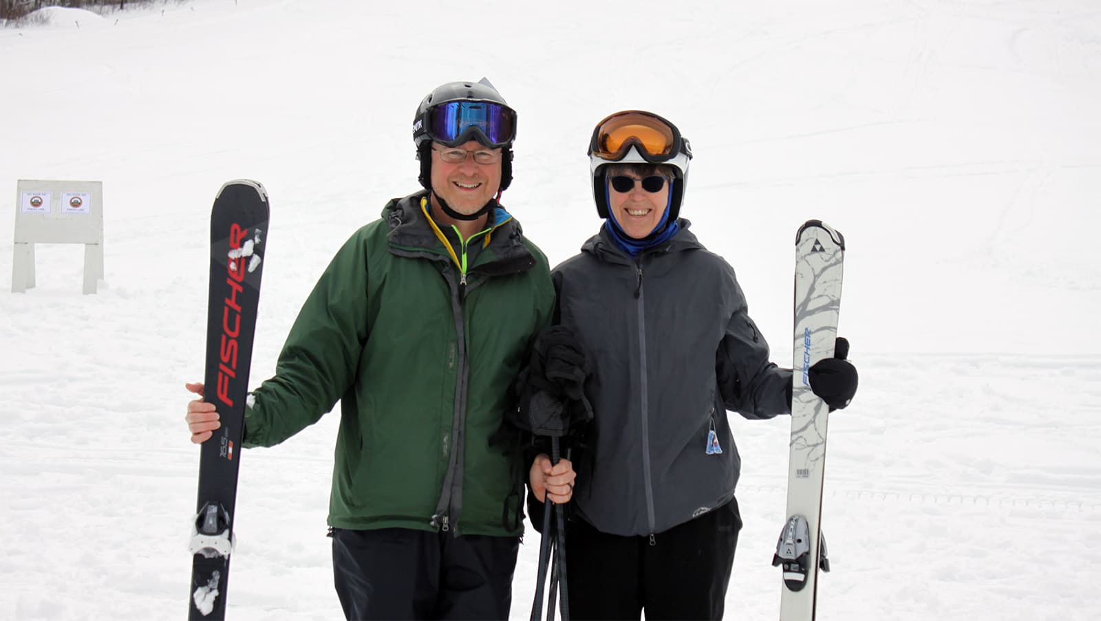 a couple smiles while posing holding their skis at the end of the downhill ski leg of the event