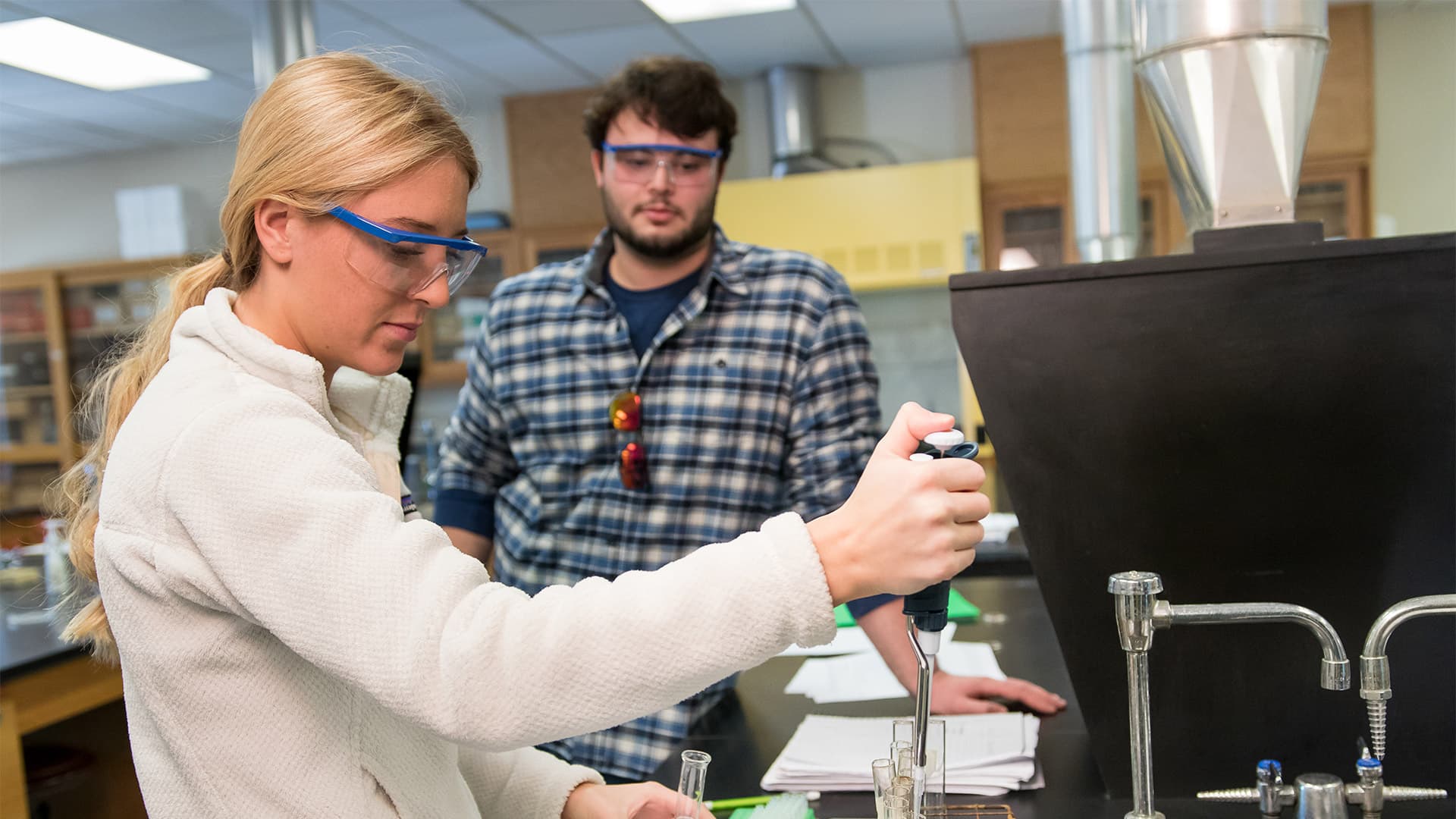 a male and female student work together in a chemistry lab performing an experiment