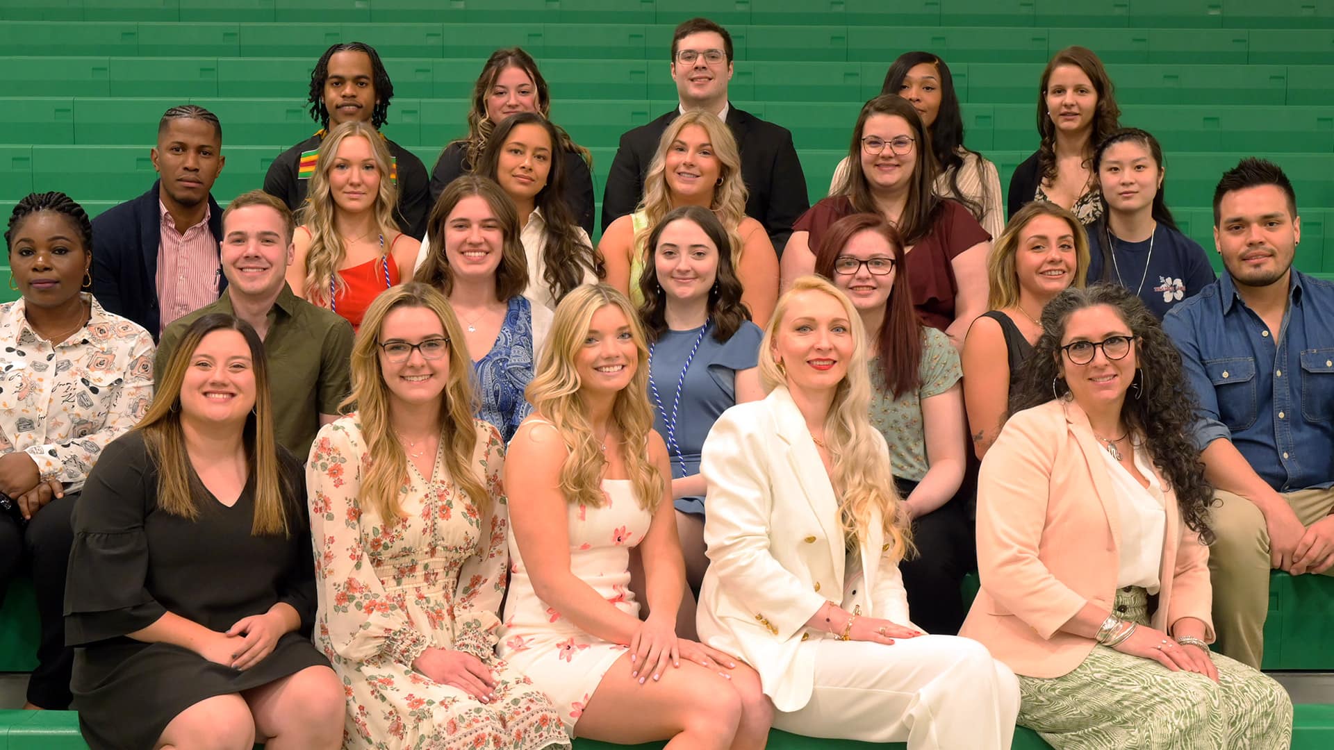 a group of nursing graduates attending the pinning ceremony poses together, sitting on bleachers