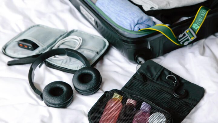 an open suitcase, music player, headphones, and toiletries placed on a bed