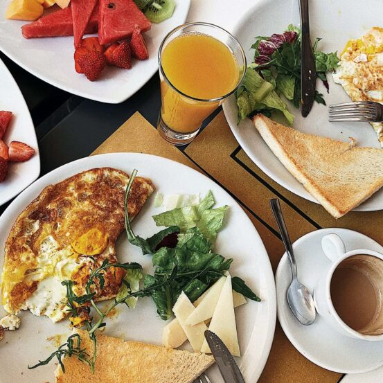 a table with plates and dishes of brunch foods consisting of eggs, toast, greens, fruit, juice, and coffee