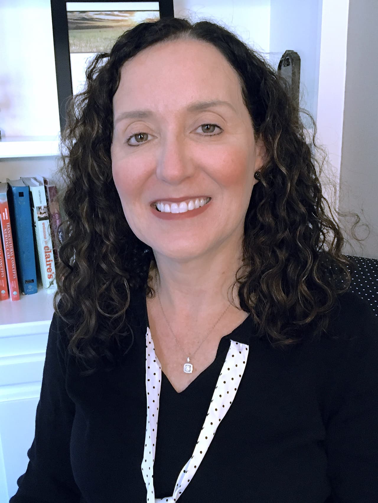 Photo of Doctor Rachel E. Albert, nursing professor and outstanding alumni award recipient. She is seated in front of a set of white bookshelves dressed in black.