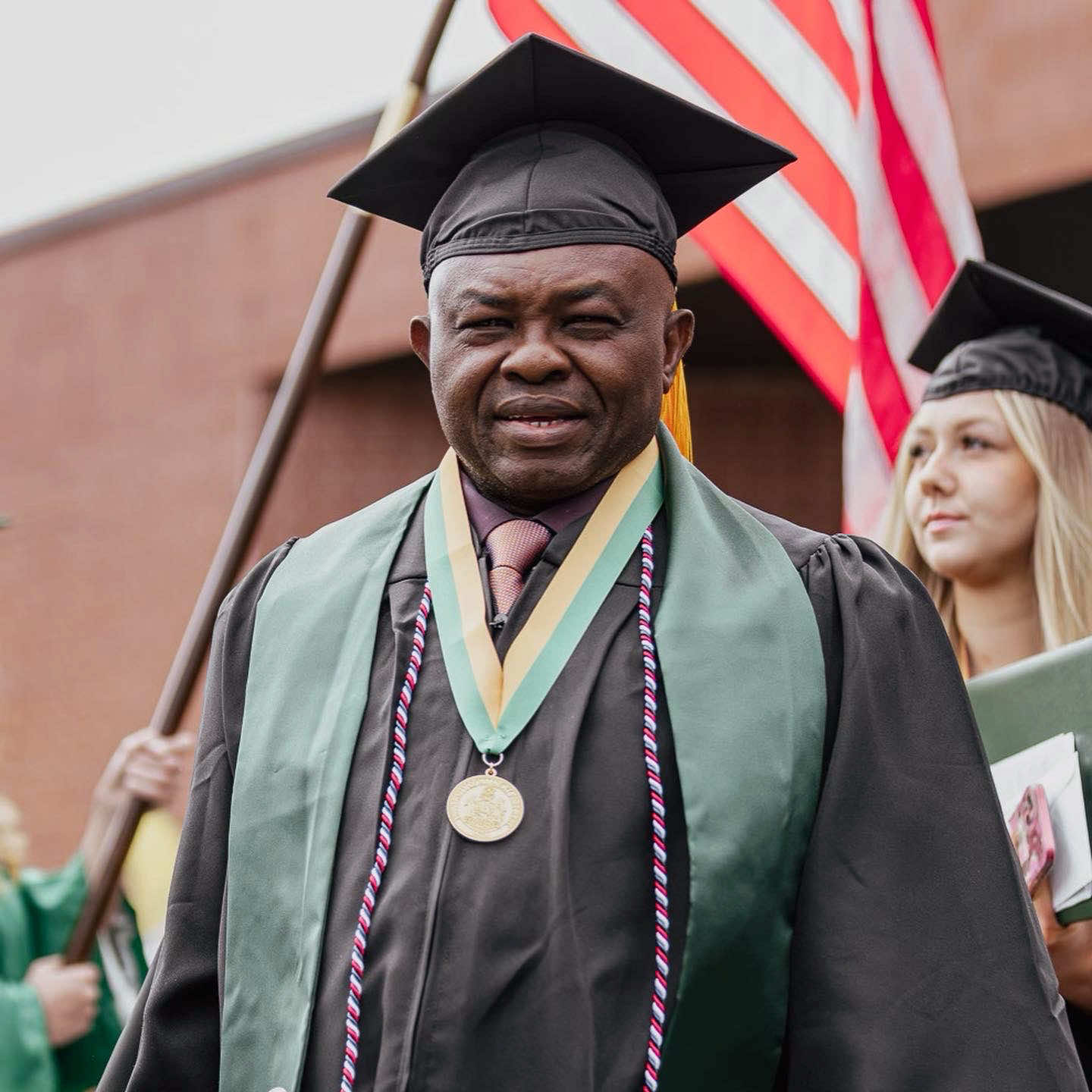 A male non-traditional recent graduate gazes at the camera as he exits the sports center after the commencement ceremony