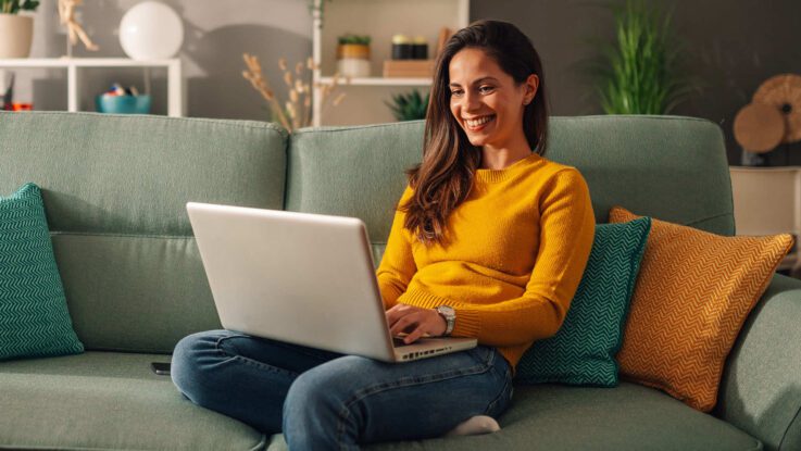 a female student sits on a couch with her laptop