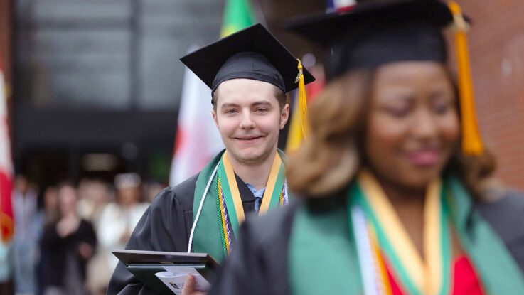 a male graduate walks out of the Sports Center after commencement