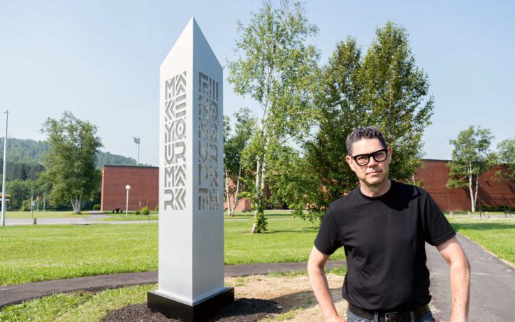Artist Robert Brochu stands next to the landmark sculpture he created for UMFK