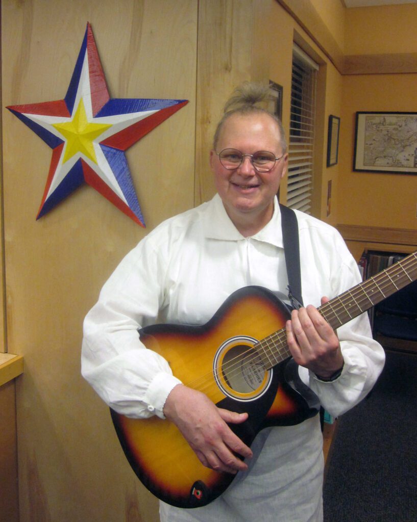 Dr. Scott Brickman poses holding an acoustic guitar