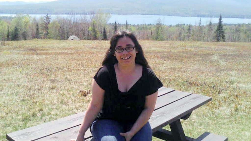 Stacy Laliberty sitting on a picnic table in front of a view of Mount Katahdin