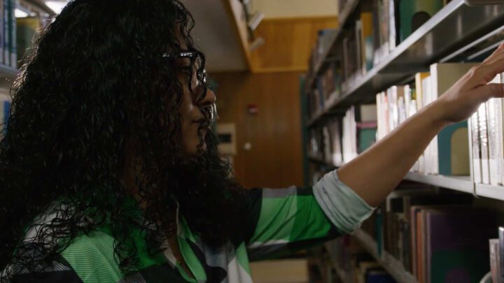 a female student stands in Blake Library looking at books on the shelves