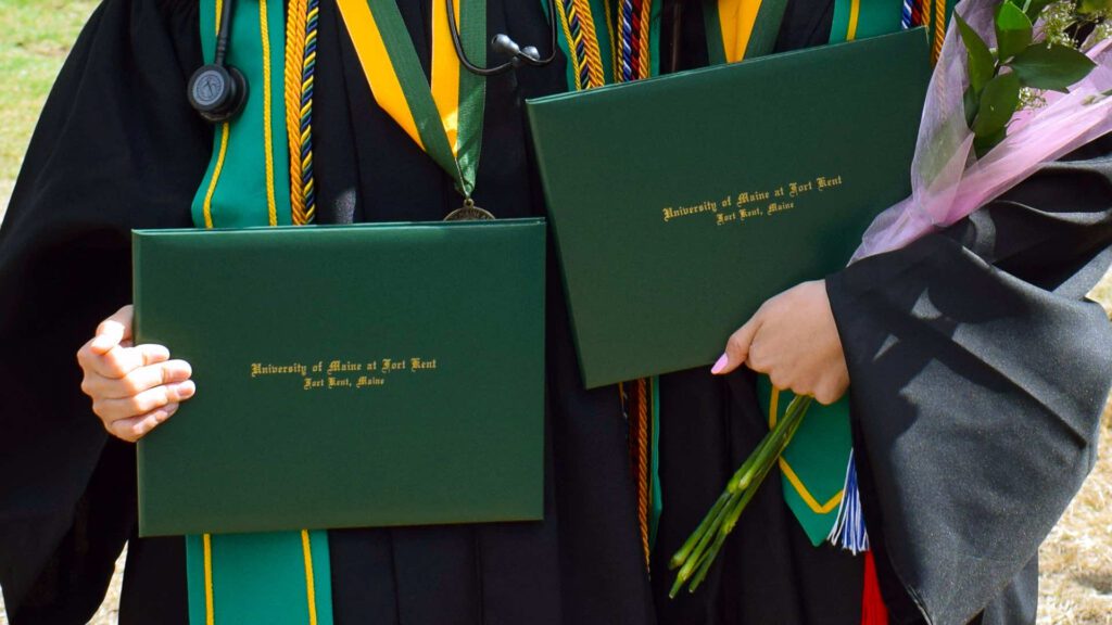 two graduates pose holding their diplomas