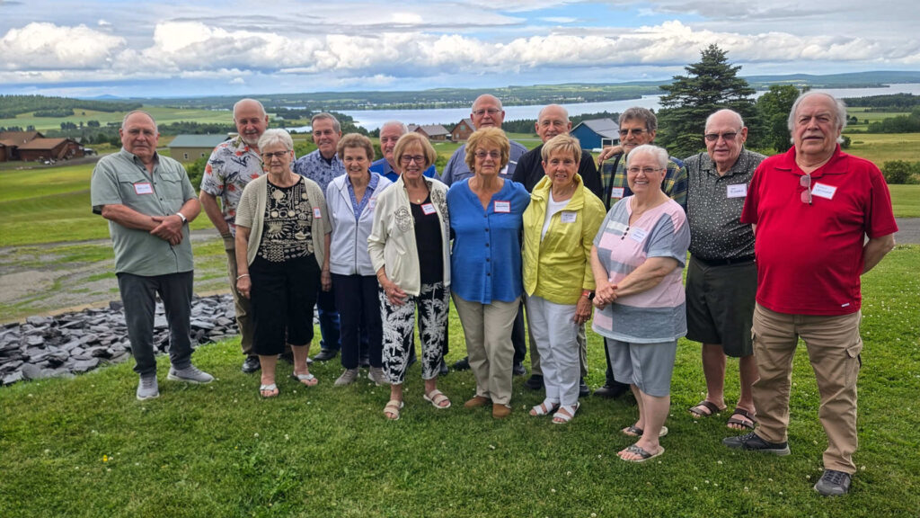 15 members of the Fort Kent Community High School class of 1961 stand together outside for a group photo